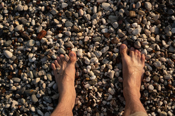 Bare men's feet standing on wet pebbles. Texture
