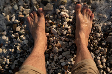 Sea foam washes men's feet standing on a pebble beach