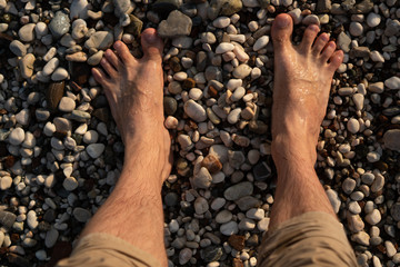Bare men's feet standing on wet pebbles. Texture