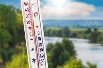 The thermometer on the background of the summer landscape shows 25 degrees of heat_