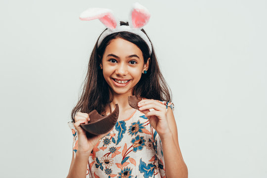 Sweet little girl wearing bunny ears eating chocolate Easter egg. Easter in Brazil