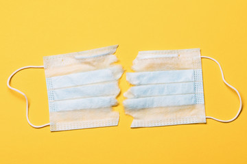 Torn in half medical mask on a yellow background, top view