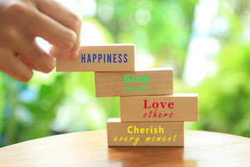 Inspirational single kind word on wooden blocks - happiness, give thanks, love others, cherish every moment. With young woman holding one wood block of happiness. Life with colorful positive word. - obrazy, fototapety, plakaty