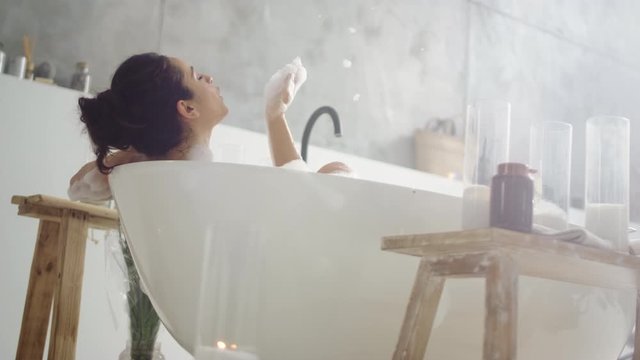 Close up sensual woman blowing foam. Smiling girl having fun with foam in bath.