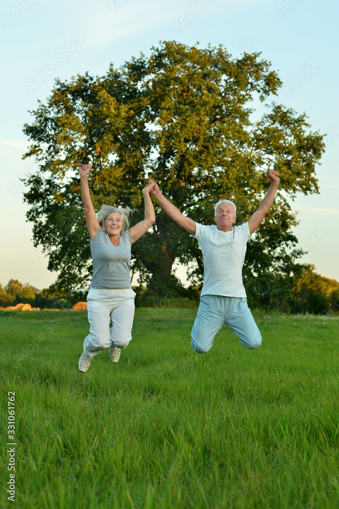 Sticker Portrait of fit senior couple jumping in park