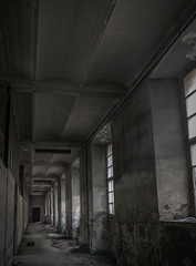 Pasillo de fabrica abandonada con ventanales en la penumbra.