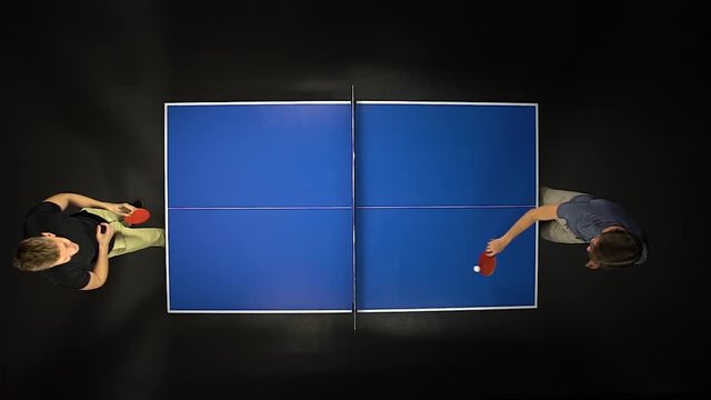 Two young men playing ping pong game enjoying competitive sport in dark background. Top view. Slow motion