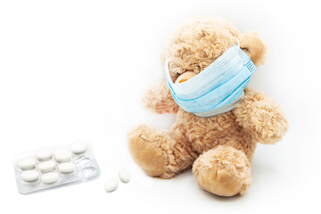 Teddy bear with protective medical mask with the pills isolated on a white background.	
