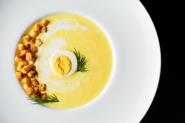 Cream soup with cheese, egg,  spices, fried croutons, in a white round plate on a black background