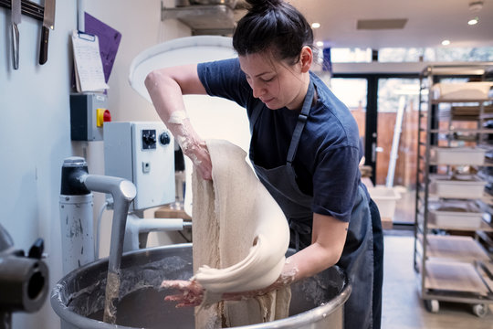 Woman wearing apron standing in an artisan bakery, working with sourdough.