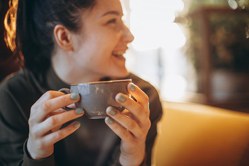 young pretty girl with a big mug of sweet coffee sits on a chair in her favorite cafe and drinks her daily morning coffee and talks with a girlfriend