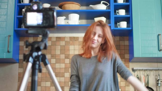 Girl food blogger influencer is recording a video or podcast in the kitchen. Dancing in front of the camera, having fun with subscribers.