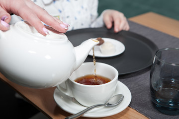 Family Tea Party. Black tea is poured into a tea cup from a white teapot. Close-up