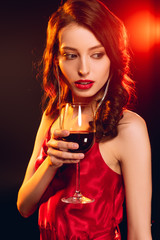 Beautiful woman in red dress holding glass of wine on black background with lighting