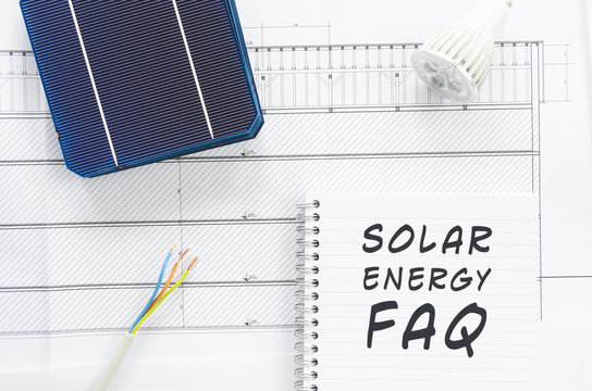 Solar cells, wires and led bulb in conceptual image with FAQ written on note pad.