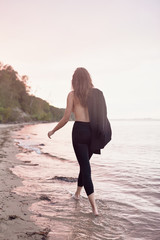 beautiful naked young and athletic girl walking on the beach with a black suit, sea sunset, lifestyle and fashion