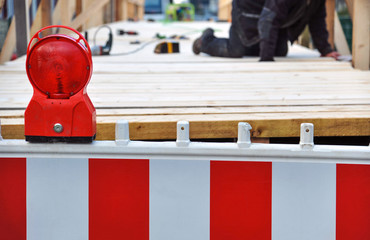 Abgesperrte Baustelle mit rot-weißer  Barke, Baustellenlampe und einem Arbeiter unscharf im Hintergrund - selektiver Fokus