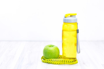 green apple, measuring tape, water bottle on a light wooden background. weight loss and sports concept