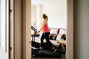 Beautiful caucasian blonde woman exercises on a treadmill in her living room