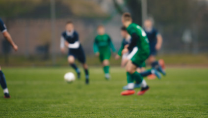 Blurred background of soccer players kicking match on grass pitch. Blurred football athletes running after ball