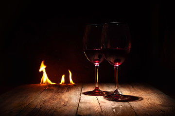 Romantic evening background. Two wineglasses with red wine in front of a warm fireplace. Copy space.