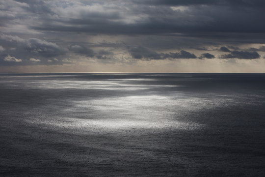 Storm clouds clearing over expansive ocean, dappled sunlight on water, northern Oregon coast,Clearing storm clouds and dappled sunlight on vast ocean at dusk
