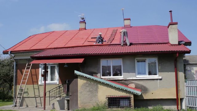 two men paint the roof,young man helps senior man to paint roof on house in village