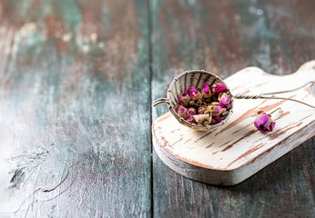 Buds of tea rose for tea in a vintage strainer on a on a dark wooden background.