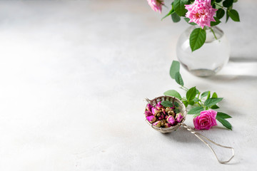 Buds of tea rose for tea in a vintage strainer on a light background.