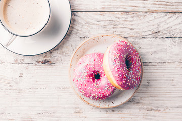 Morning coffee cup and sweet pastry of strawberry donut on rustic white wooden table. Top view....