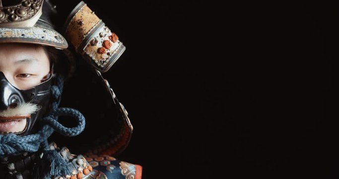 Japanese man in traditional samurai armor and authentic helmet looking at camera, isolated on black background - close up portrait shot 4k footage