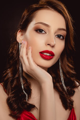 Fototapeta premium Portrait of beautiful woman with red lips touching face and looking at camera isolated on black