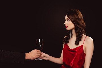 Side view of man giving glass of red wine to elegant girl isolated on black