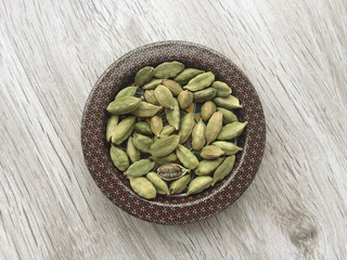 Dried green organic cardamom pods in dish on wooden table, closeup and top view.