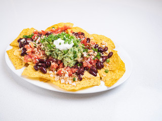 Nachos Traditional Mexican dish. Fresh tasty homemade food for lunch. Balanced and healthy meal. Mexican food nachos with meat beans guacamole and sour creme. Eat healthy at home. 
