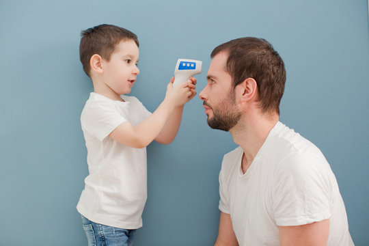 Toddler Boy Is Measuring His Father's Body Temperature Using Infrared Thermometer