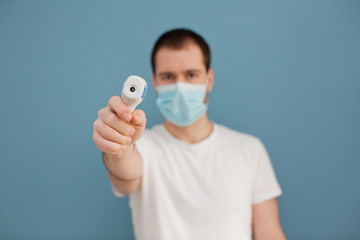 young man wearing surgical mask is using infrared thermometer