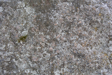 Roughly treated surface of an old reddish granite block covered with lichen