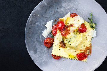 Traditionelle italienische Ravioli Pasta angeboten mit Parmesan Käse und gebratene Tomaten als Draufsicht auf einem Modern Design Teller mit Textfreiraum links