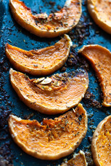 Roasted pumpkin slices seasoned with salt and herbs on a oven plate. Autumn dish top view