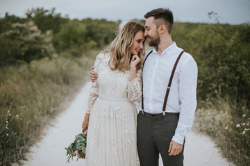 Smiling bride and groom spending time together. Posing on the mountain hills background. Dressed in white dress beautiful blonde caucasian bride and handsome groom. Hugs, kissess and enjoy the company