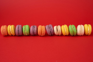 pile of multi-colored baked macarons almond flour cakes on a red background