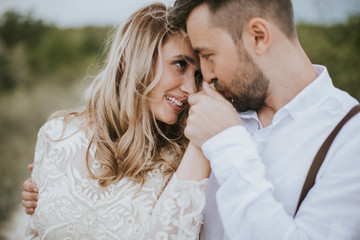 Smiling bride and groom spending time together. Posing on the mountain hills background. Dressed in white dress beautiful blonde caucasian bride and handsome groom. Hugs, kissess and enjoy the company