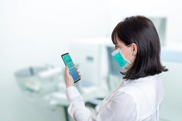 Woman in a hospital lab holds a phone with the findings of a patient who is positive for a corona...