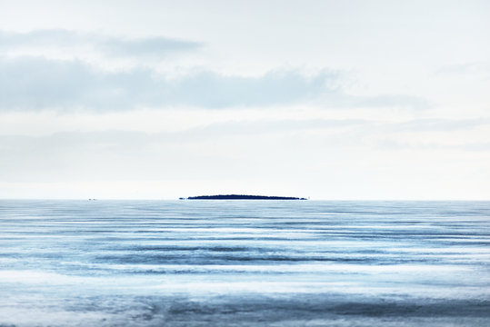 A view of the frozen Onega lake after a blizzard. An island with a lonely tree in the background. Dramatic evening sky. Stunning cloudscape. Karelia, Russia