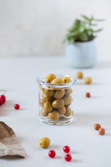 Food photo of green olives in a glass jar on a light background, nuts and a green plant. There is a place for text.