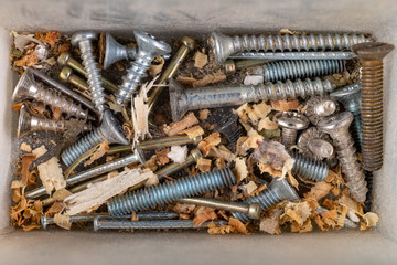Bolts and screws in a plastic container. Screws dirty with sawdust.
