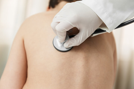 latex gloved hand of a female doctor with a phonendoscope (stethoscope) on a child's back to listen. in the hospital bed or home. home doctor. medical inspection.