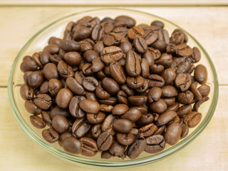 Coffee beans in a glass plate on a wooden background