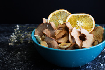 On a dark background, fruit chips in a blue plate, chips from apples, pears and oranges